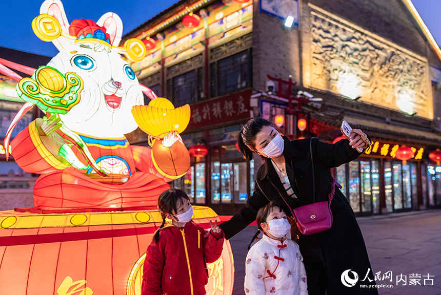 1月18日晚,呼和浩特市玉泉區(qū)塞上老街歷史文化街區(qū),家長(zhǎng)陪伴孩子在“福兔賀春”花燈前拍照打卡。丁根厚攝