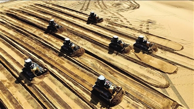 在騰格里沙漠的阿拉善盟光伏新能源+生態(tài)治理和防沙治沙光伏風(fēng)電一體化項(xiàng)目的施工現(xiàn)場(chǎng),百輛推土機(jī)征戰(zhàn)騰格里沙漠。
