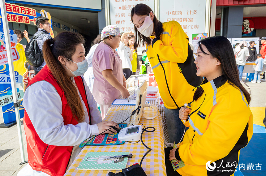 醫務志愿者在呼和浩特市玉泉區“‘新’心攜手 基層共治”游園會活動現場為外賣員進行微量元素檢測。丁根厚攝