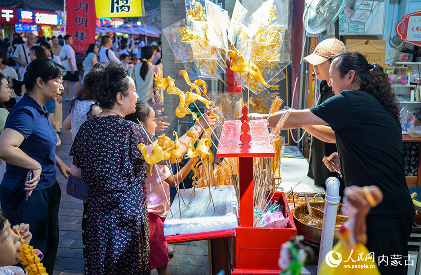 游客在呼和浩特市玉泉區(qū)塞上老街旅游休閑街區(qū)選購非遺糖畫。丁根厚攝