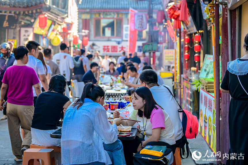 游客在呼和浩特市玉泉區塞上老街旅游休閑街區“通順大巷夜市”品嘗特色小吃。丁根厚攝