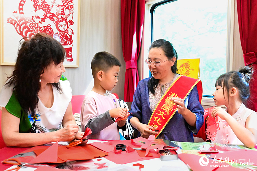 8月10日，非遺傳承人張燁楠（右二）在“阿爾山號”旅游專列上向游客傳授剪紙技藝。王正攝