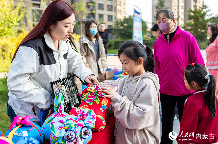 呼和浩特市玉泉區“文明市集”主題活動現場，工作人員為小朋友講解“敕勒川巧娘”布老虎手工藝品的制作技藝。丁根厚攝