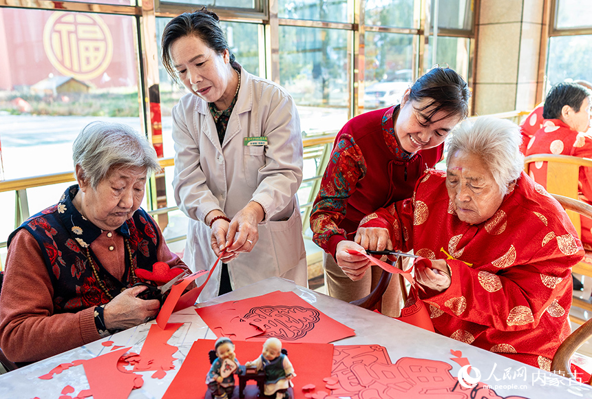 護理員陪伴老人們在呼和浩特市玉泉區民政局“愛心敬老 情暖重陽”主題活動現場一起剪紙。丁根厚攝