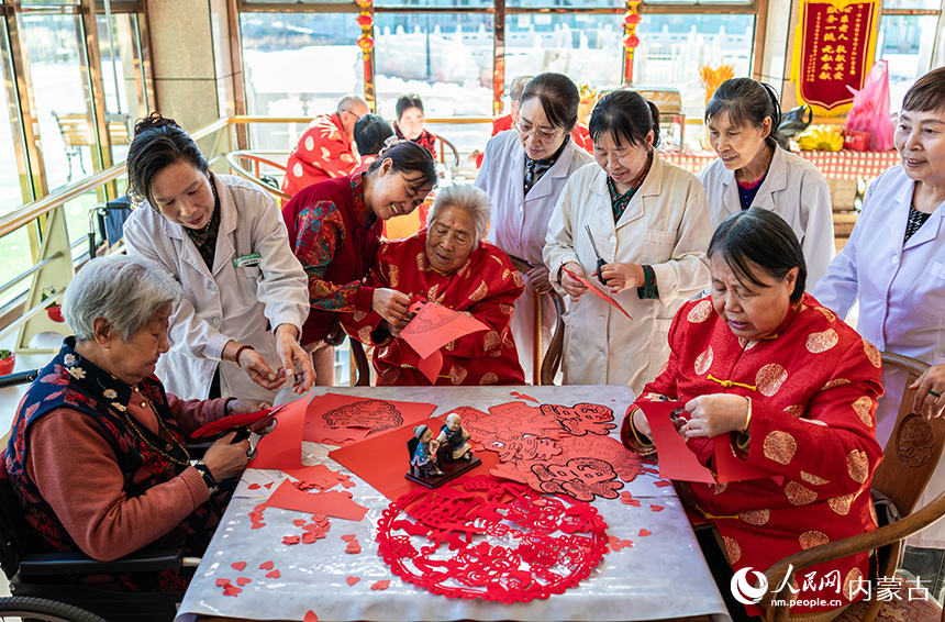 護理員陪伴老人們在呼和浩特市玉泉區民政局“愛心敬老 情暖重陽”主題活動現場一起剪紙。丁根厚攝