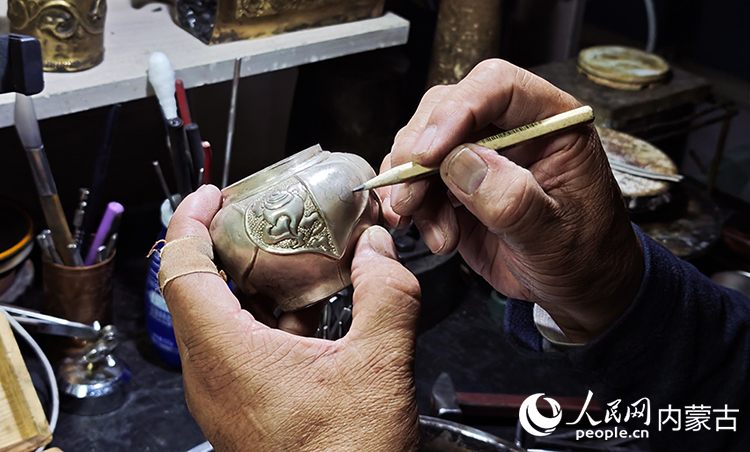 國家級非物質文化遺產代表性項目烏拉特銅銀器制作技藝傳承人巴圖陶高對需要鏨刻的銀壺設計圖案。人民網記者 張雪冬攝