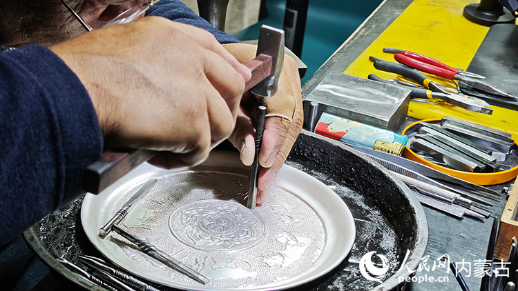 國家級非物質文化遺產代表性項目烏拉特銅銀器制作技藝傳承人巴圖陶高對制作的銀盤進行鏨刻。人民網記者 張雪冬攝